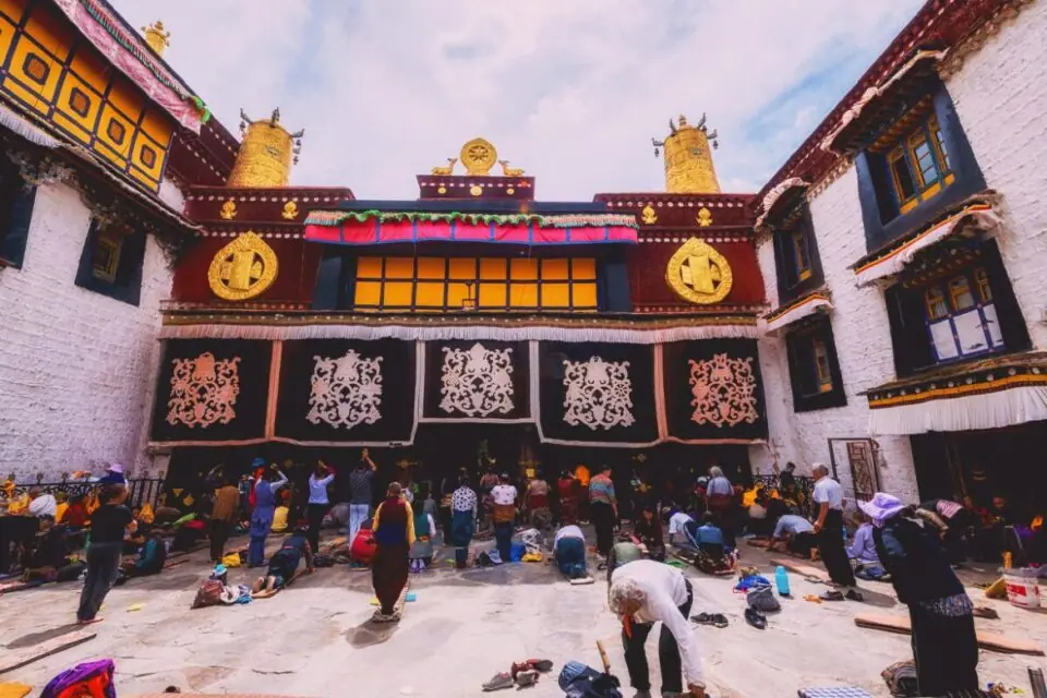 Pilgrims prostrating in the courtyard of the Jokhang Temple in Lhasa, beneath its gilded roof ornaments