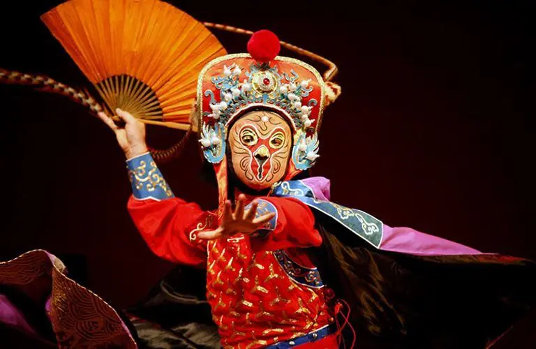 A Sichuan opera face-changing performer in a painted mask and red costume, fan raised