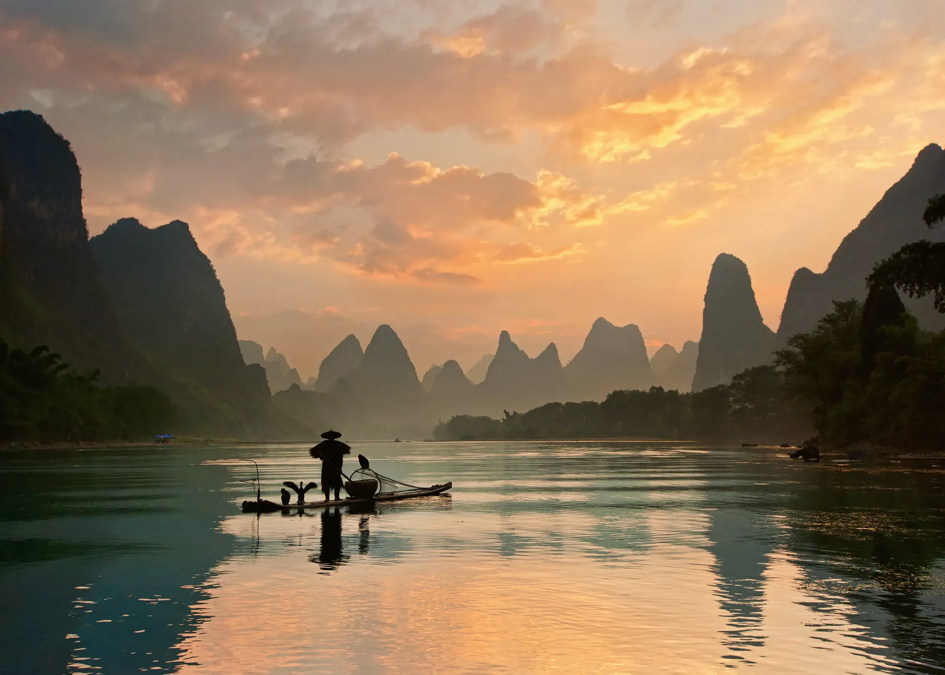 A fisherman on a bamboo raft on the Li River at sunset, karst peaks behind