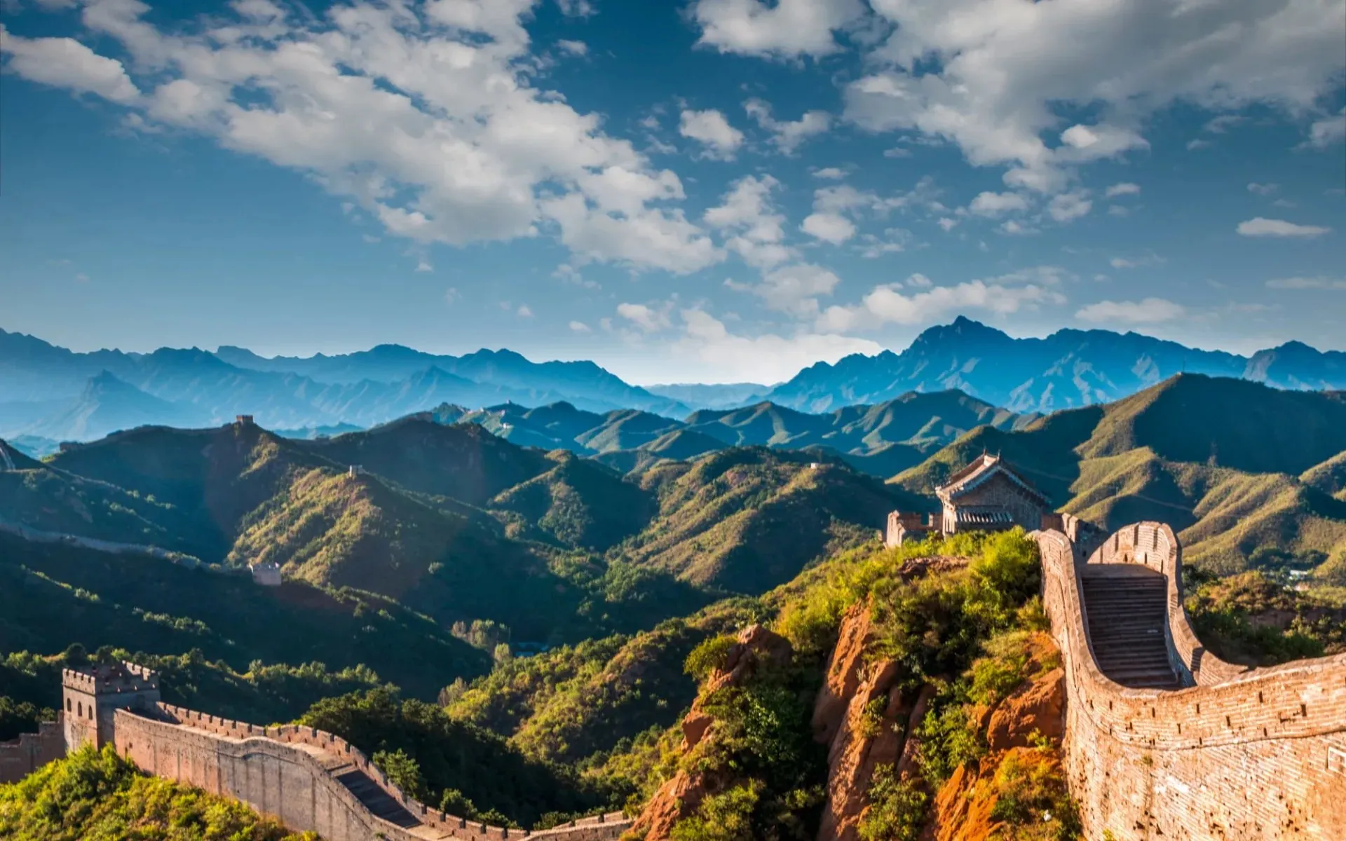 The Great Wall winding over green mountain ridges under a bright sky