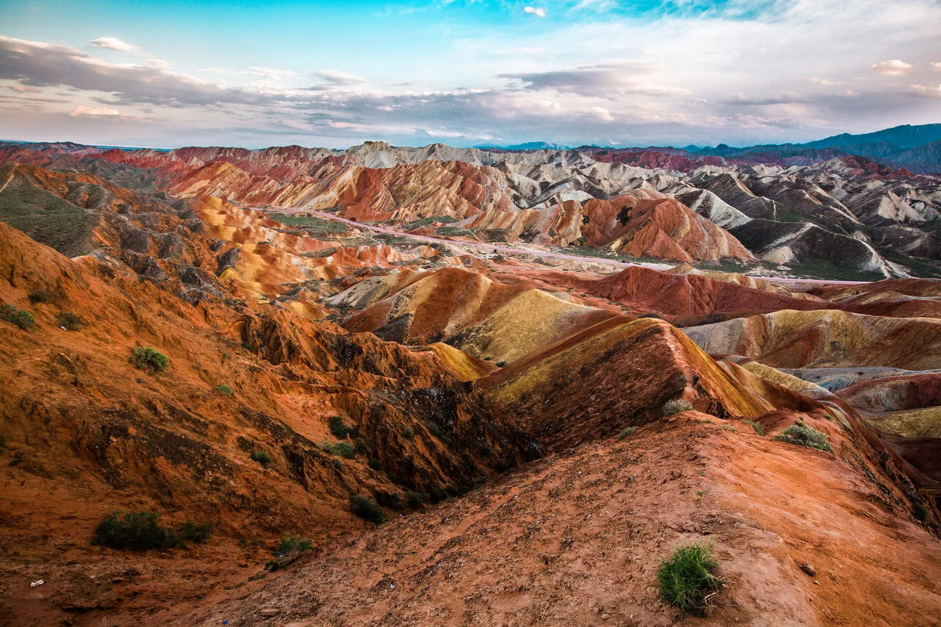 The rainbow-striped Danxia hills at Zhangye in Gansu — layered red, orange and ochre ridges under a wide sky, on the Hexi Corridor road trip