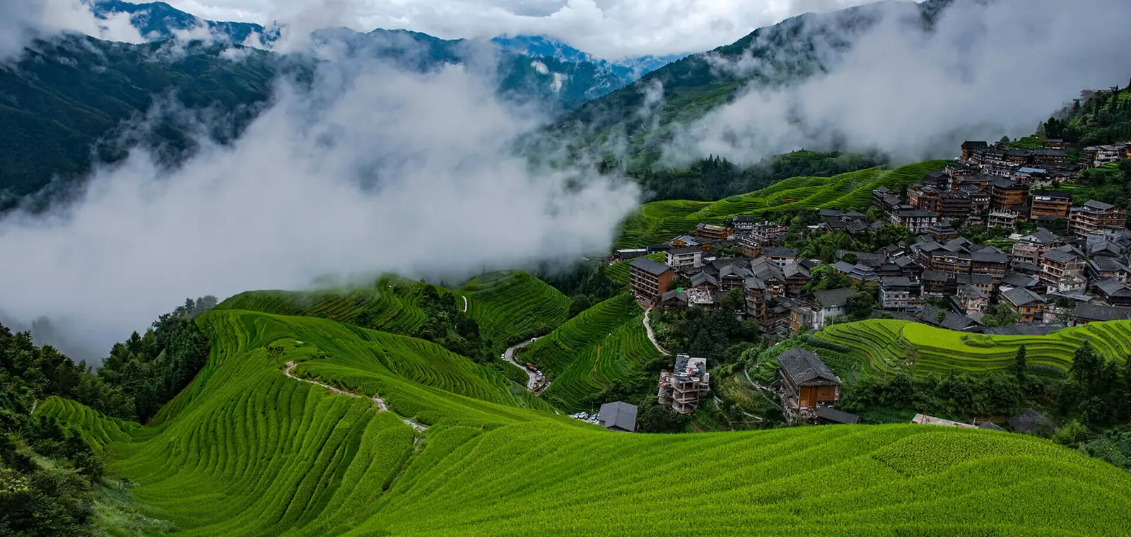 The Longji rice terraces curving around Ping'an village in Guangxi, mist drifting through the valley below
